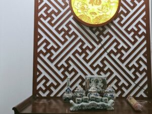 Bàn thờ gia tiên trong căn hộ chung cư với vách ốp gỗ hoa văn, đèn hào quang tròn và bộ đồ thờ gốm men lam
